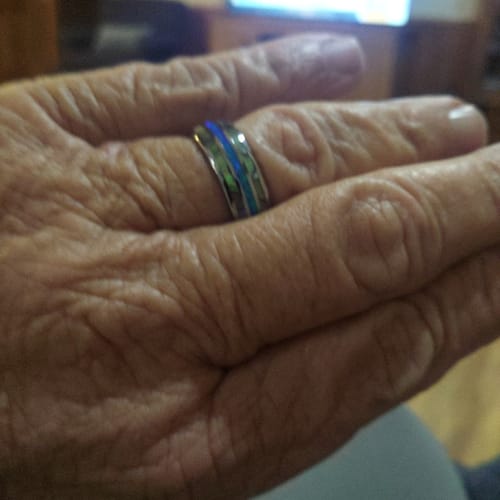 Close-up of a customer's hand wearing the Vanguard ring, showing the blue opal and abalone inlays.