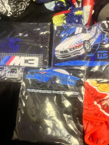Customer shows three graphic t-shirts from the TCG89 Black Friday Mystery Cash Box, still in their packaging.