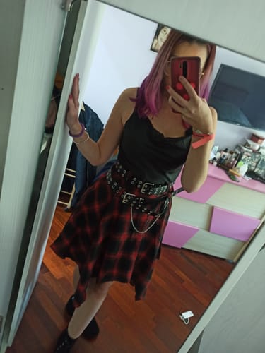 Reviewer wearing the plaid cowl neck dress, styled with multiple studded belts and a chain.