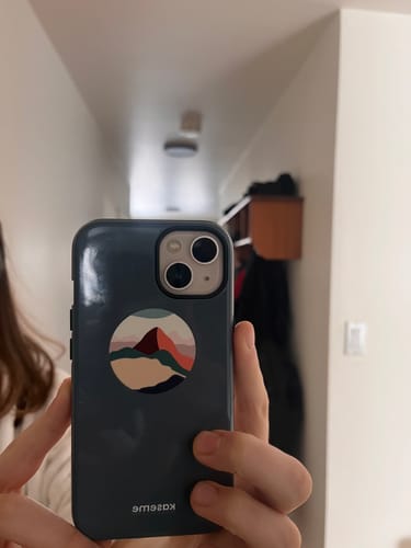 Reviewer holding their phone, showing the back of the dark grey Climb case with a stylized mountain pop socket.