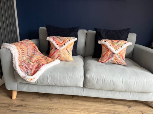 Reviewer's finished Hearthside Rainbow Blanket and two matching cushions with white fur trim, displayed on a sofa.