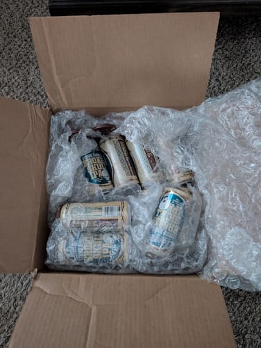 Customer's view of beer cans wrapped in protective bubble wrap inside an open shipping box.