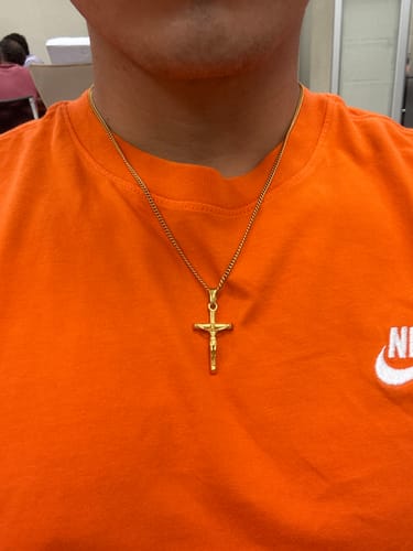 Primer plano de un cliente que lleva el Colgante Cross Minimal Oro sobre una camiseta naranja.