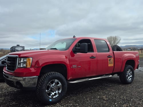 Customer's red GMC truck after installing the Suspension System, showing its raised height and new tires.