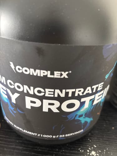 Close-up of the reviewer's black tub of Complex CFM Whey Concentrate Protein.