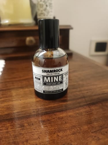 Cliente mostra la boccetta di profumo SHAMROCK appoggiata su un mobile di legno.