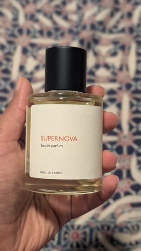A customer holds their bottle of Supernova Eau de Parfum, showing the simple white label and black cap.
