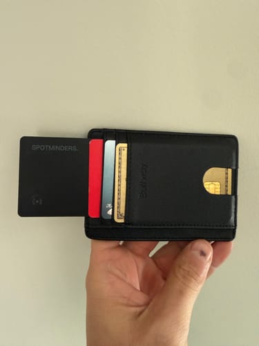 Customer holding a black wallet, showing the SPOTMINDERS tracking card partially inserted next to other cards.