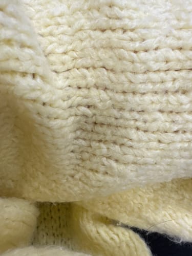 Rezensent zeigt eine Nahaufnahme der groben Stricktextur des hellgelben Bouclé Oversized Cardigans.