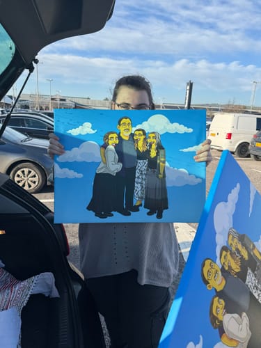 Customer holding a large canvas showing their custom 'Turn Me Yellow' hand-drawn family portrait outdoors.