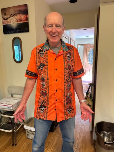 Customer's front view of the orange Que Vivan Los Muertos Guayabera shirt featuring calavera and instrument patterns.