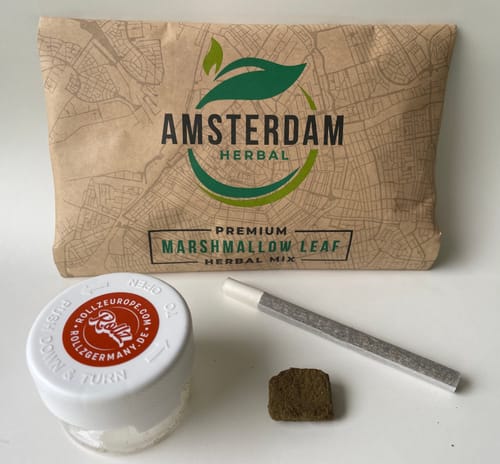 Customer's THC-A 45% Hash La Mousse, a small brown block, with a pre-rolled cigarette and herb packaging on a table.