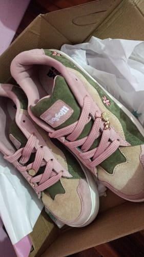 Customer's Blossom sneakers in pink and green suede, featuring floral charms, resting inside the product box.