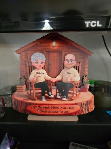 Customer's personalized wooden cabin plaque sitting on a television, featuring two cartoon-style figures.