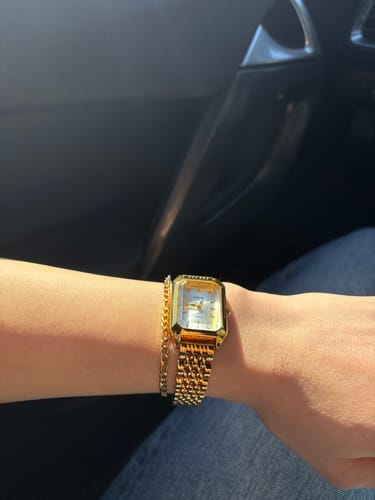 Reviewer's gold Claire De Mains watch with a metal link strap worn on their wrist, next to a thin gold bracelet.