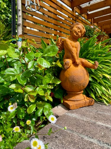 Customer's rust-finish Hugo Wingsley cherub statue placed in a leafy garden setting.