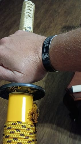 Customer's custom black bracelet worn on the wrist while gripping the yellow handle of a sword.