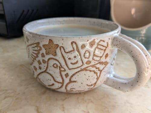 Reviewer's wide, handmade Annie's Potteries x Bird Collective mug featuring etched pigeon and city icon designs.