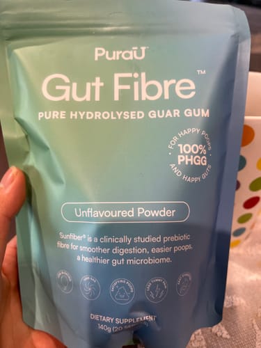 Customer's hand holding a blue PuraU Gut Fibre pouch with clear text about pure hydrolysed guar gum.