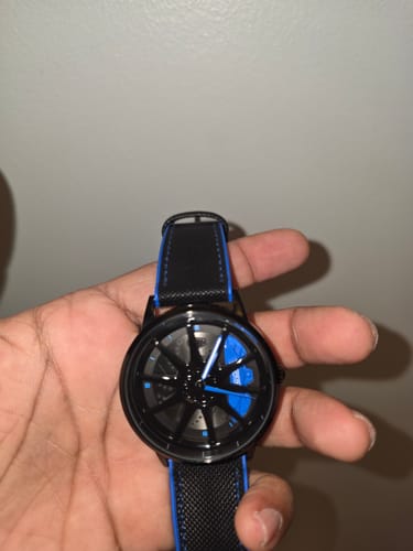 Customer's HMN BRZ Performance watch held in hand, featuring a black wheel face and vibrant blue hands and stitching.