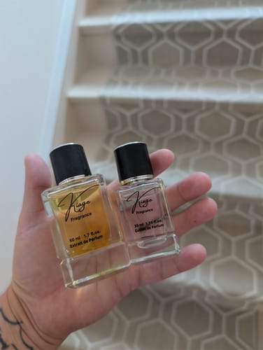 Reviewer's hand holding two glass bottles of Kiage fragrance against a patterned staircase.