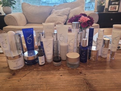Reviewer's Alastin Gentle Cleanser surrounded by many other skincare bottles on a wooden table.