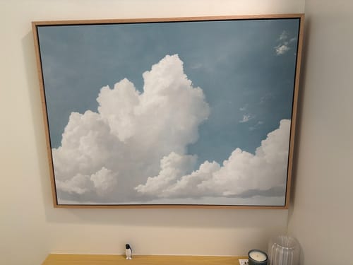 Customer's Soaring Peace canvas art featuring blue sky and clouds, mounted on a wall above a small table.