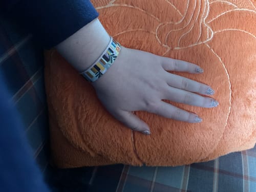 Reviewer's arm wearing the Endless Adventures Bracelet, resting on a fuzzy orange pumpkin pillow.