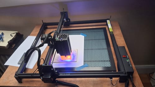 Customer's AtomStack A20 Pro V2 laser engraver positioned on a wooden table, actively cutting a piece of paper.