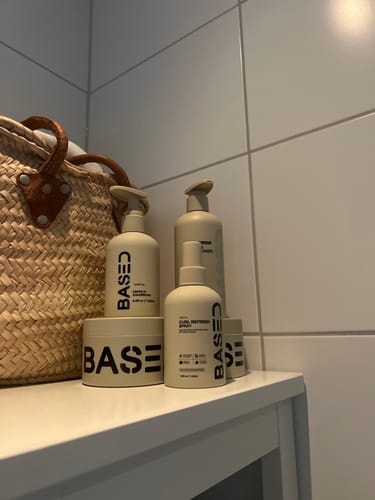 Customer's Curl Gel bottles and containers with neutral labels arranged on a bathroom shelf next to a woven basket.