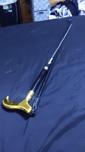 Customer's Black and Gold Gent Sword Cane with the sword blade extended, laid flat on a dark surface.