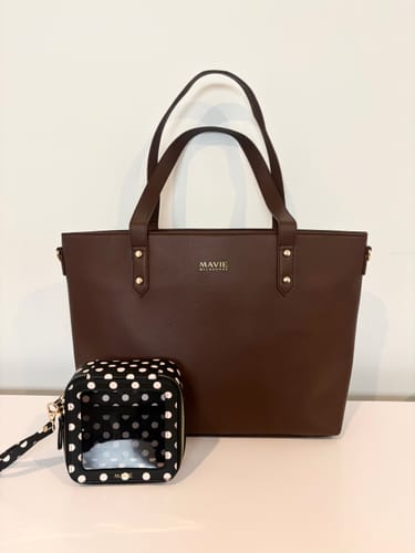 Customer's The One Tote dark brown bag with gold branding standing next to a small black polka dot pouch.
