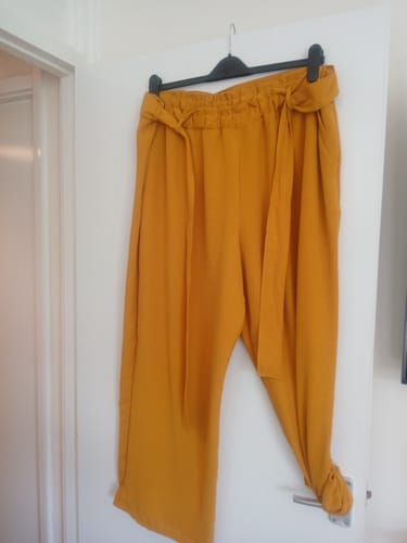 Reviewer's mustard yellow wide leg trousers made from the linen look polyester fabric, hanging on a black hanger.