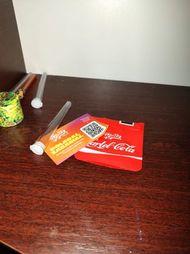 Reviewer's THC-A Pre-Roll Cali Blend packaging and clear plastic joint tubes placed on a dark wooden surface.