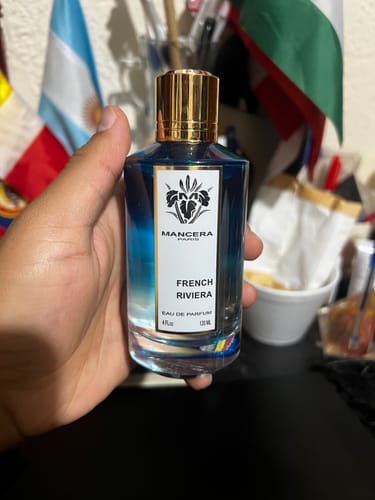 Reviewer's hand holding a blue glass bottle of Mancera French Riviera perfume with a gold cap.
