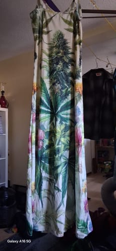 Customer's HER.B Garden Long Spaghetti Strap Dress hanging indoors with an all-over floral and marijuana leaf print.