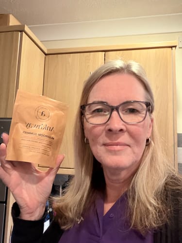Customer holding a tan Ankhway Mushroom Gummies pouch while smiling in a kitchen.