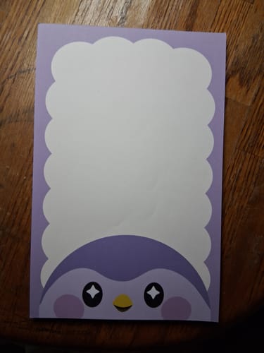 Customer's purple Finch character notepad with a cute bird face and scalloped writing space, sitting on a wooden desk.
