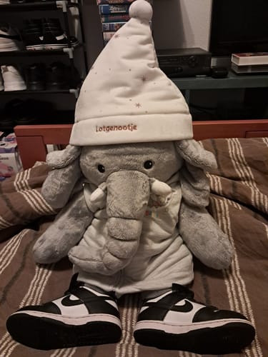 Customer's Lotgenootje Olifant knuffel met een witte muts en zwarte sneakers, zittend op een bed.