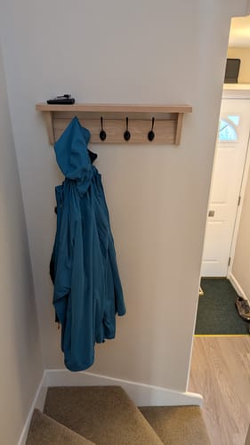 Customer's Solid Oak Walnut Coat Rack with Shelf mounted in a stairwell, with a blue jacket hanging on a hook.