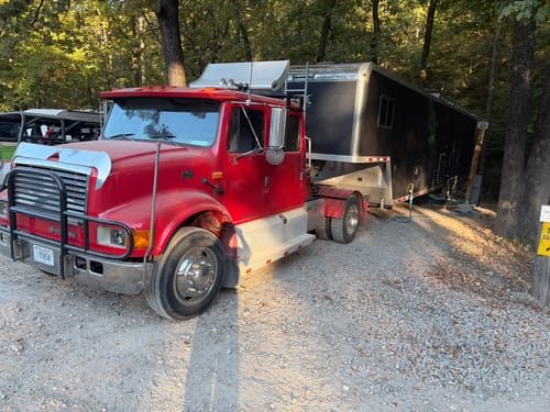 Customer's red truck equipped with the Orion Reflash System, towing a large trailer in a wooded, gravel campsite.