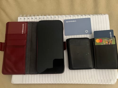Reviewer's three Spotminders Tracking Cards, in maroon and blue, resting on a notepad with phones and wallets.