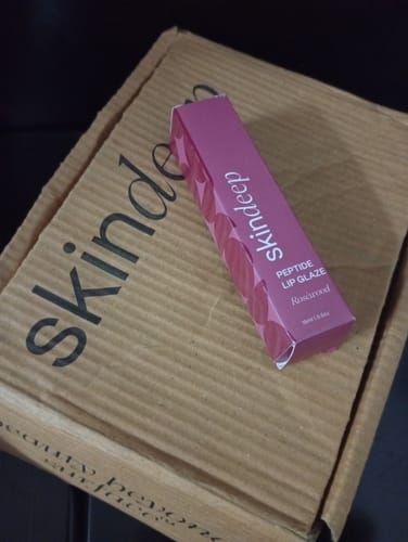Customer's Skindeep Peptide Lip Glaze product box resting on top of a cardboard delivery shipping box.