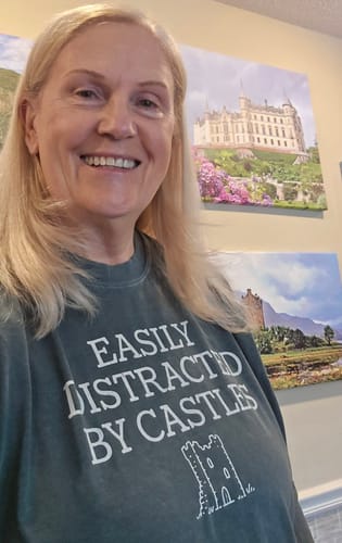 Customer's Distracted By Castles long sleeve tee in green, worn by a smiling person with castle wall art in background.