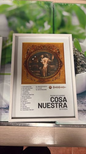 Customer's Cosa Nuestra poster framed in white on a surface with a green patterned background.