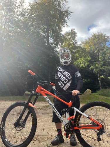 Customer's Mountain Bike Jersey worn by a person standing with an orange mountain bike outdoors in a wooded area.