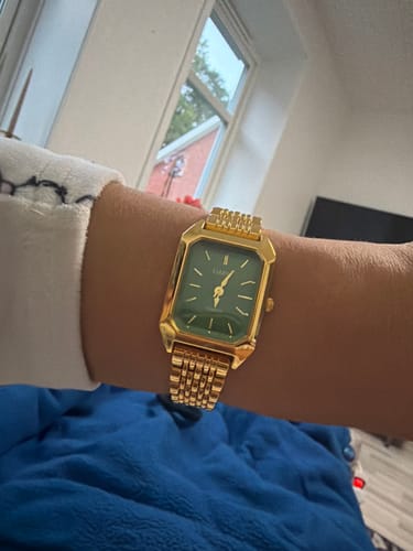 Customer's gold Claire De Mains watch with a green face worn on their wrist.