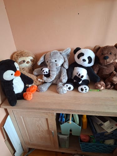Customer's grijs gekleurde Lotgenootje Olifant knuffel die rechtop op een houten kast staat tussen andere knuffeldieren.