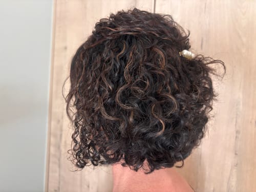Customer's dark wavy hair styled with Crème De La Curl Creme, showing defined, hydrated curls from behind.