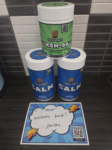 Customer's UglyFace KSM-66 and two Calm bottles on a dark tiled surface with a handwritten note from the team.
